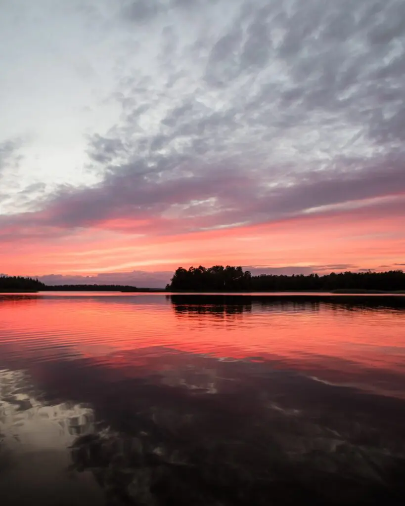 vibrant pink and orange sunset over a calm lake with forest