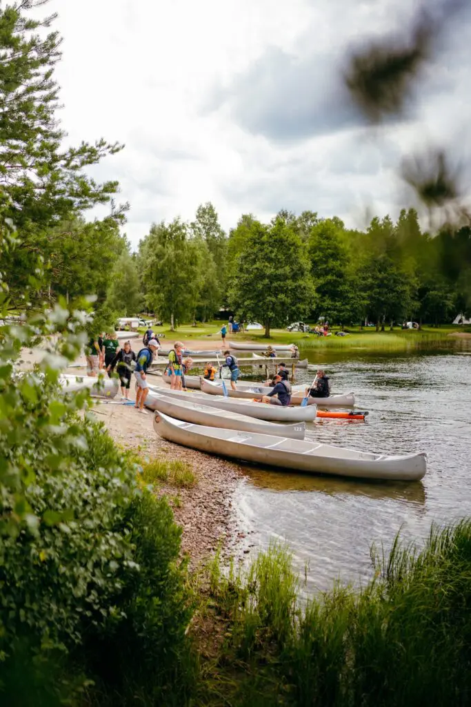 group of people preparing canoes on a lake shore