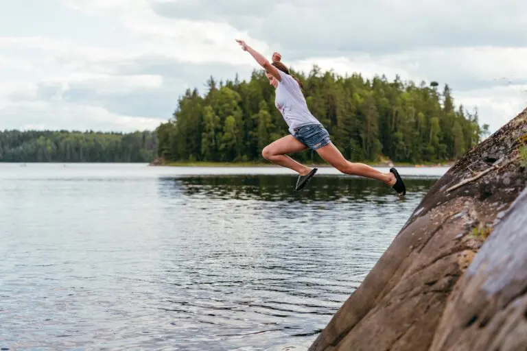 person jumping into a lake from a rock
