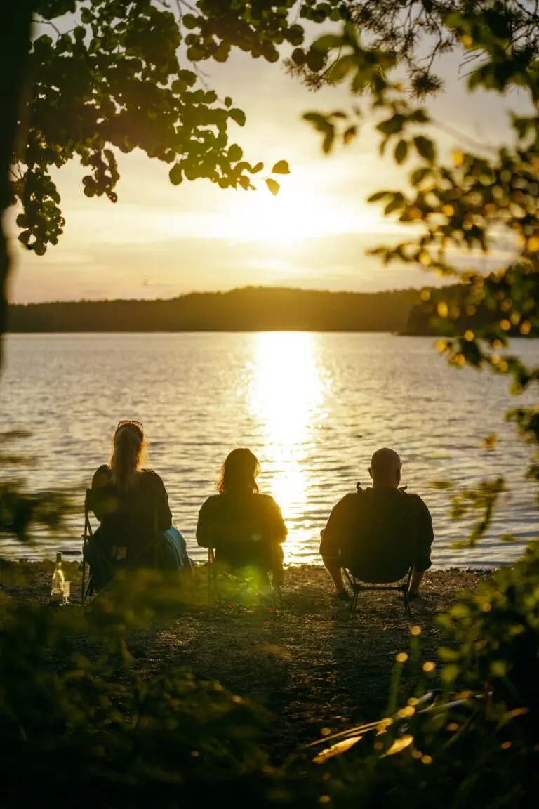 three people watching sunset over a lake from shore