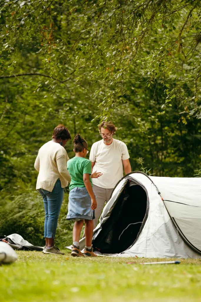 family setting up a tent in a green forest campsite