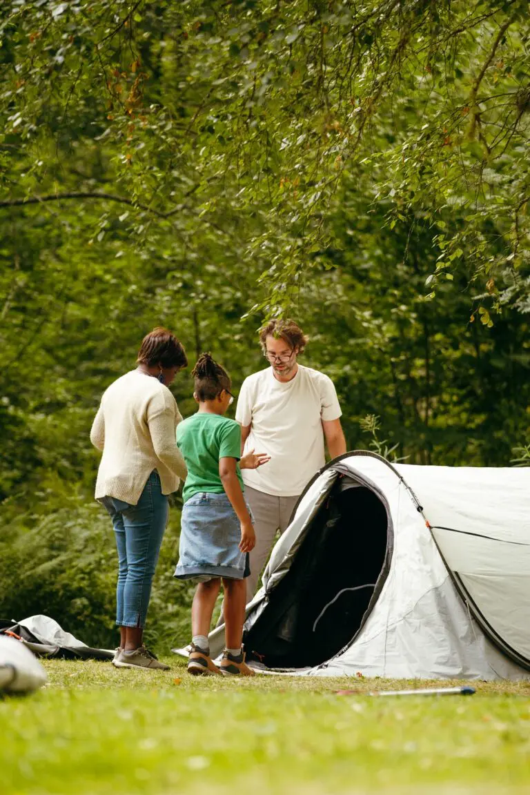 family setting up a tent in a green forest campsite