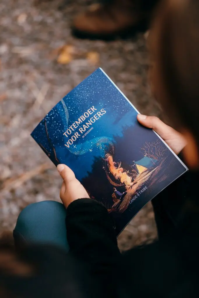 person holding a book with a starry night and campfire illustration