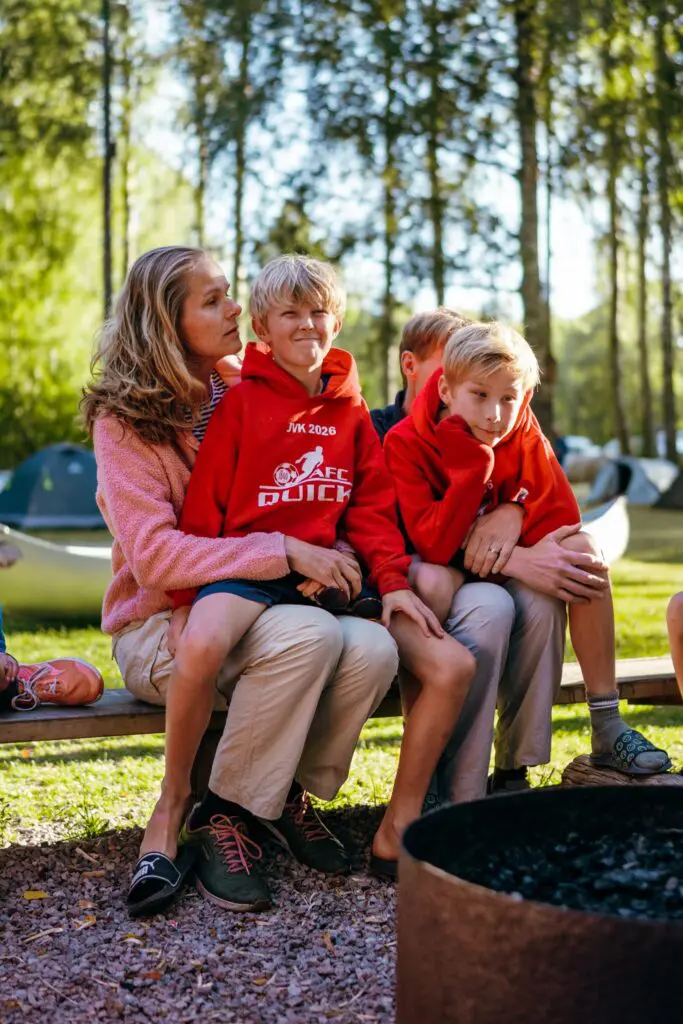 family sitting on a bench by a campfire in a forest