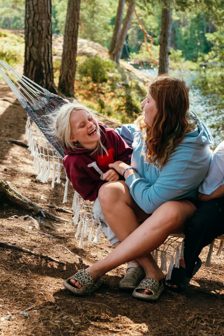 two young women laughing in a hammock by a lake