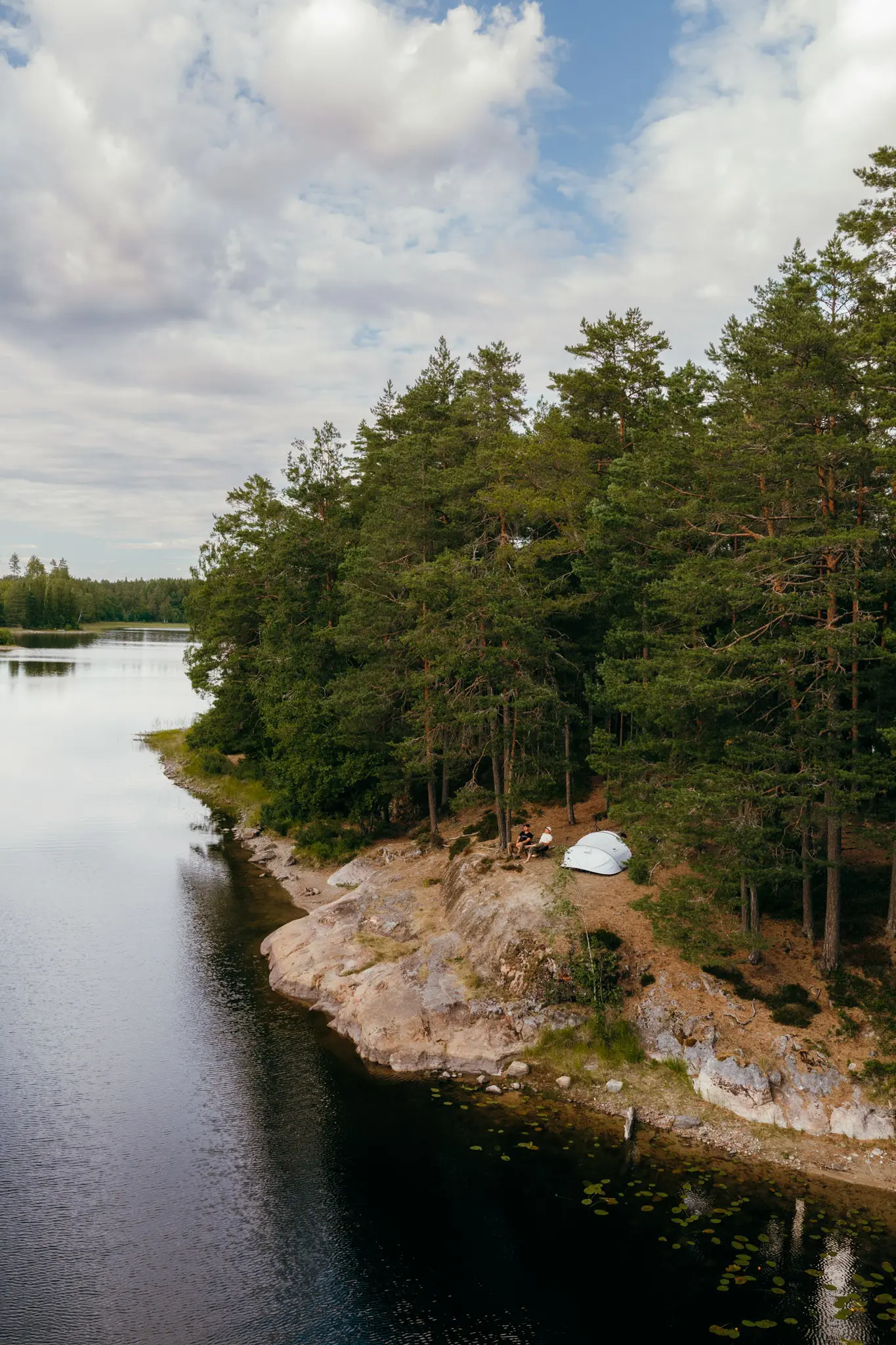 drone shot of two people camping by a lake in a forest