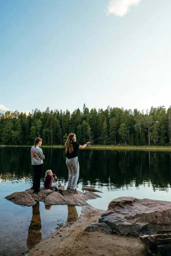 three people fishing from rocks on a calm lake