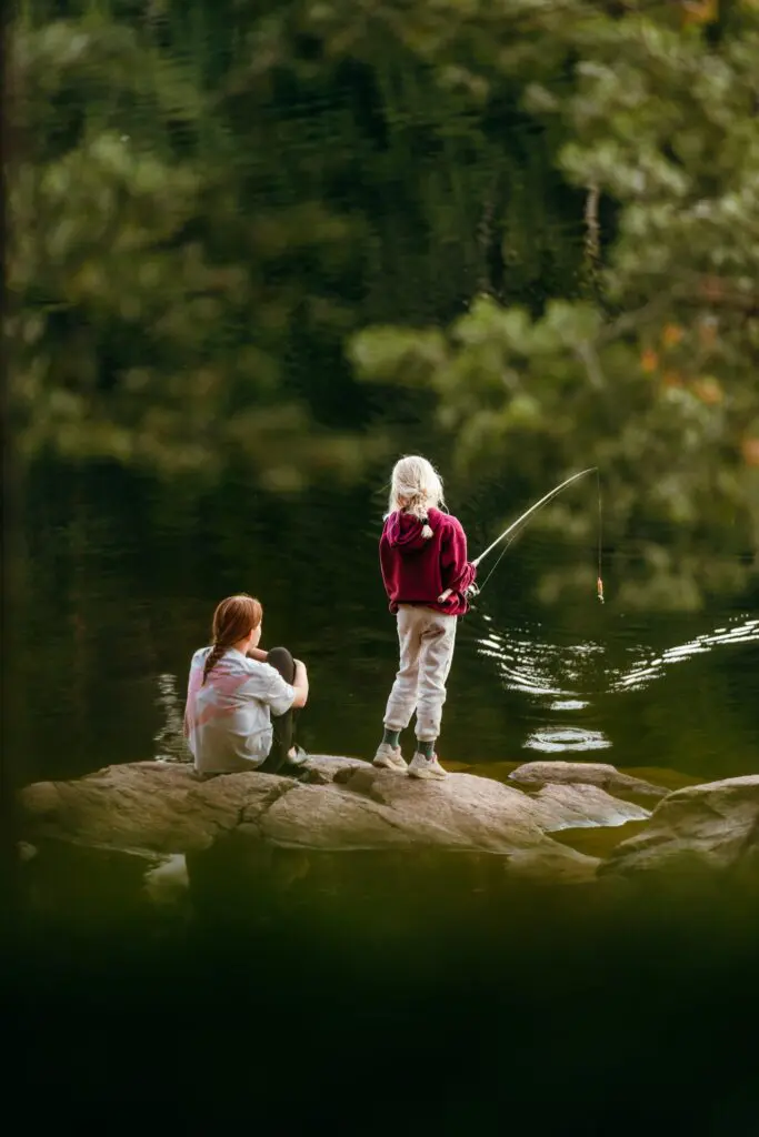 two girls fishing by a lake in a forest