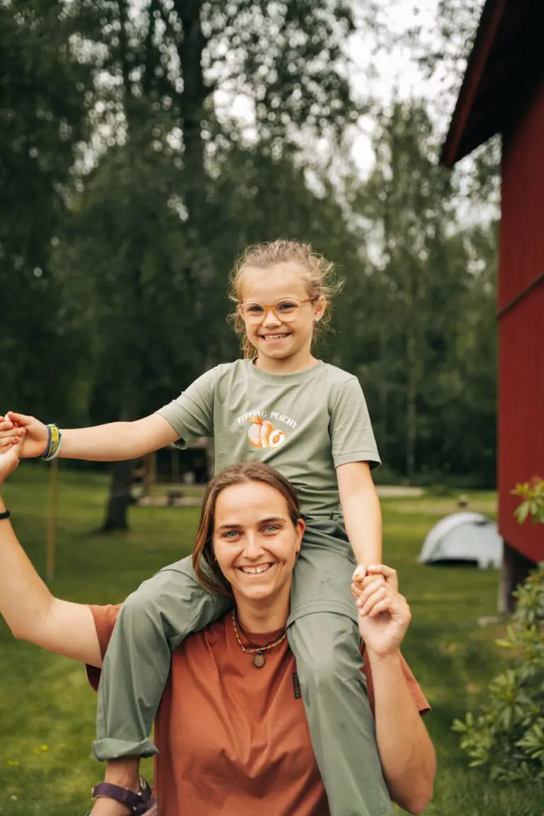 mother carrying child on shoulders, smiling outdoors