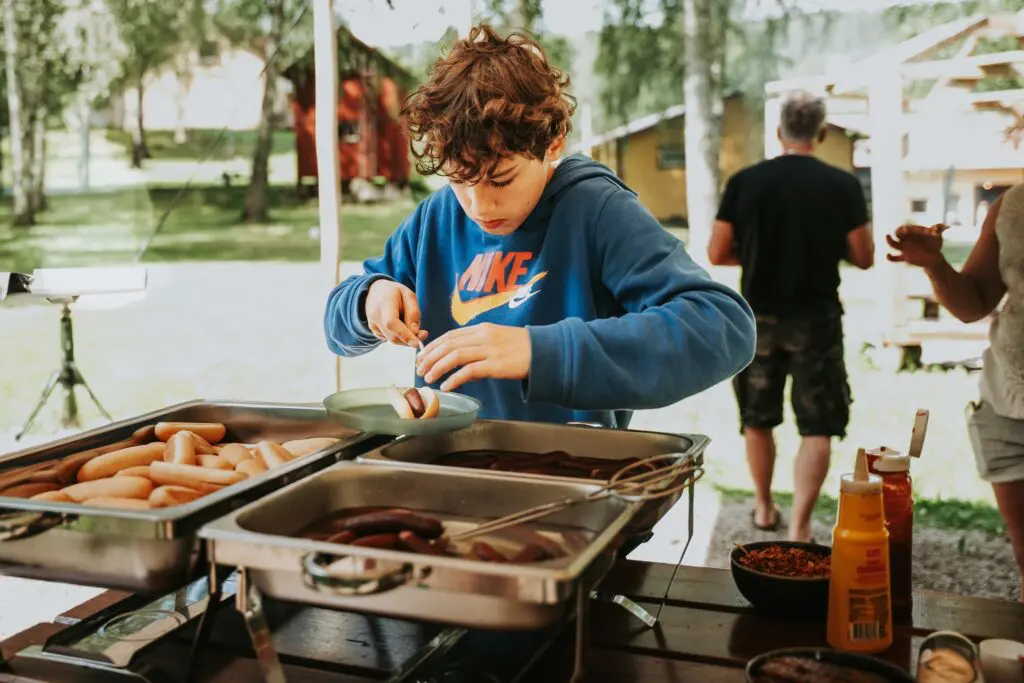 boy making a hot dog at an outdoor buffet