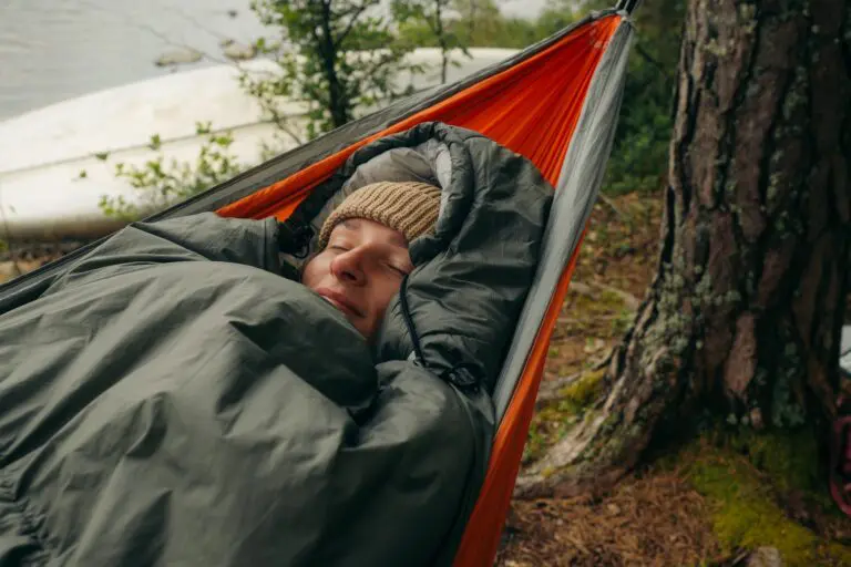 person sleeping in a hammock by a lake
