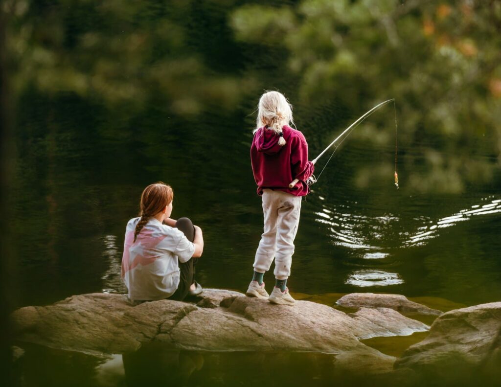 two girls fishing by a lake in a forest